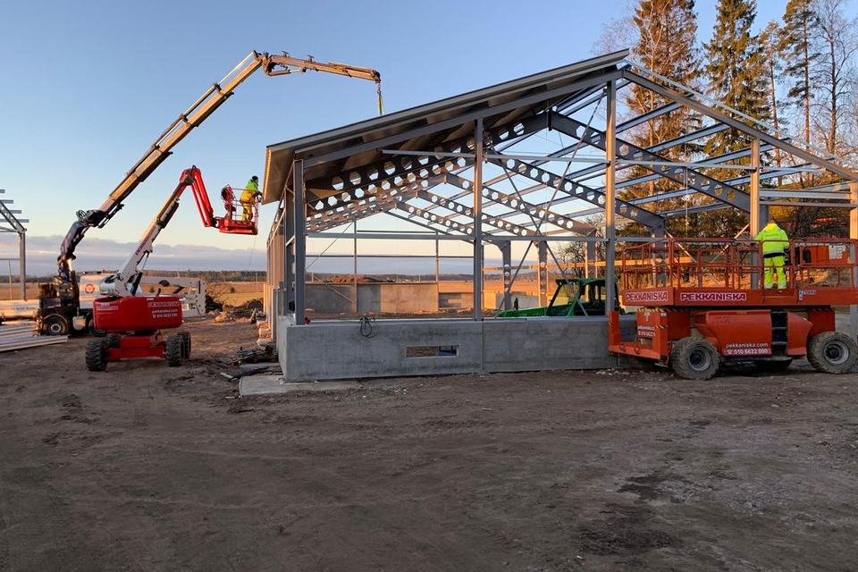 Crane and work platforms installing roof panels on a steel-framed farm building